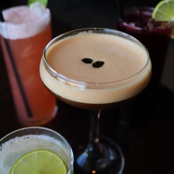 Espresso martini with coffee beans, surrounded by other colorful cocktails.