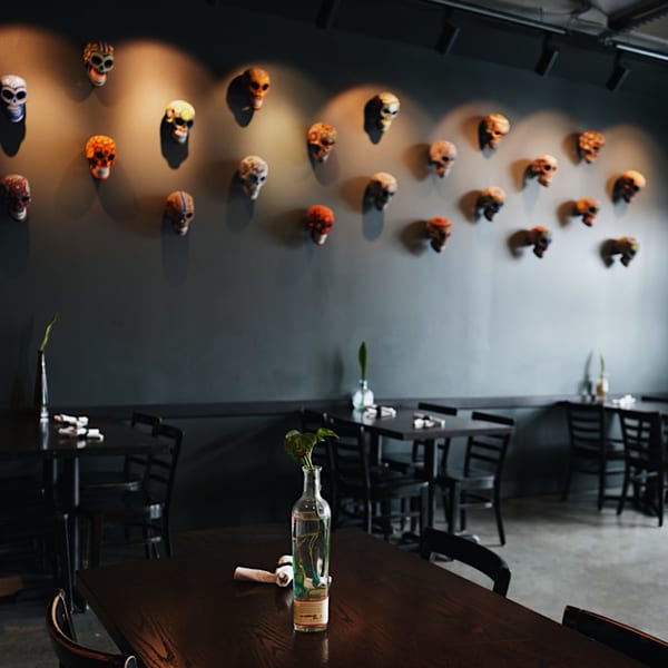 Dark restaurant interior with tables, chairs, and a wall adorned with decorative skulls.