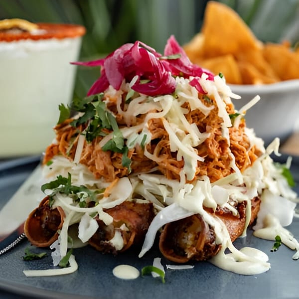 Crispy Sonora taquitos topped with shredded chicken, cabbage, pickled onions, and crema, with a margarita.