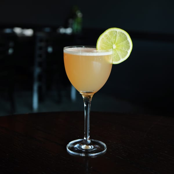 A Sonora Mexican Kitchen and Bar cocktail, garnished with a lime slice, on a dark table.