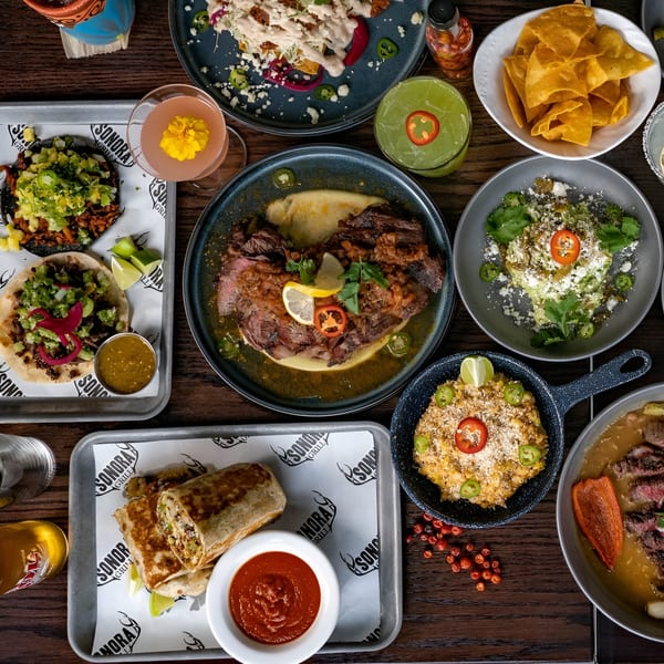 Overhead view of a table laden with various Sonora Mexican dishes, drinks, and chips.