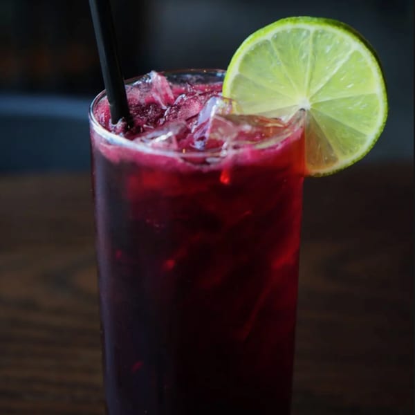 A tall glass of iced red beverage with a black straw and a lime slice garnish.