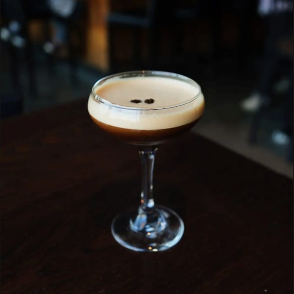 Espresso martini with foam and two coffee beans on a dark wooden table.
