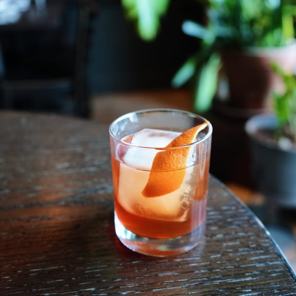 A Sonora Mexican Kitchen and Bar cocktail with an orange peel and large ice cube on a wooden table.