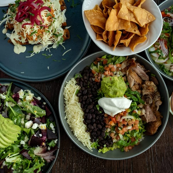 A vibrant spread of Mexican dishes, including chilaquiles, a burrito bowl, a beet salad, and tortilla chips.